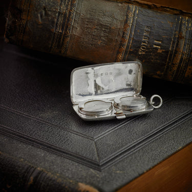 Vintage silver compact with two round lenses on an old leather-bound book