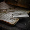 Silver pocket watch on an open book with visible text and a pen.