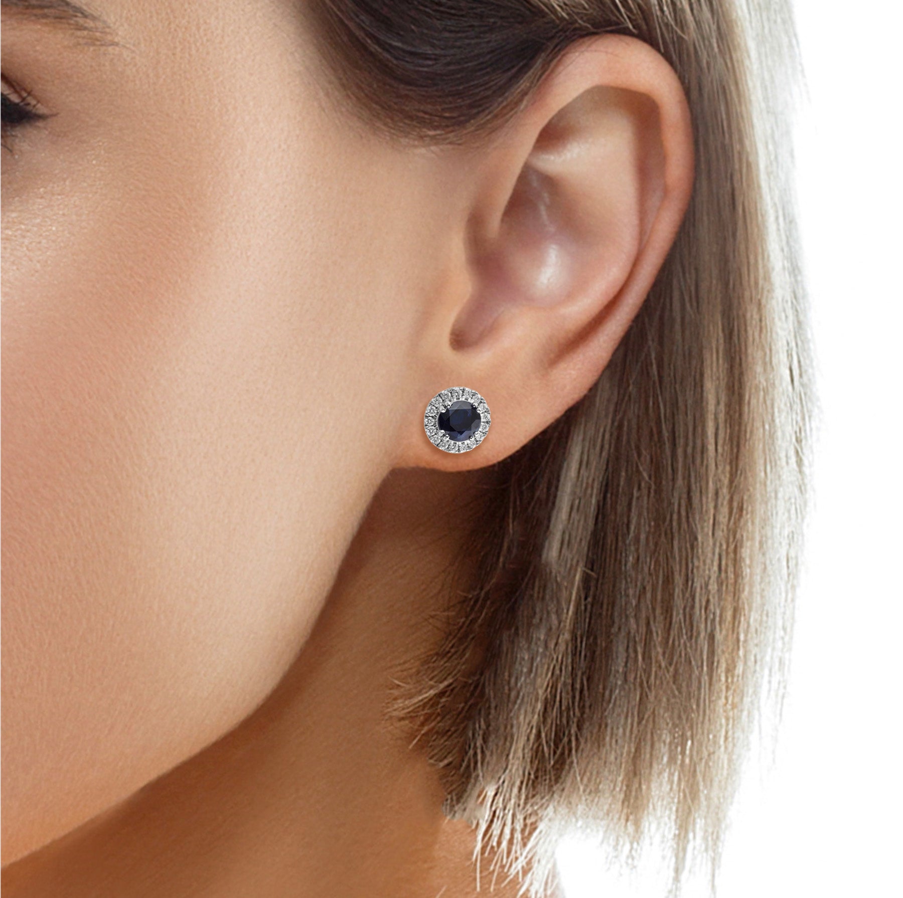 Blue sapphire and diamond halo stud earrings shown worn in the ear